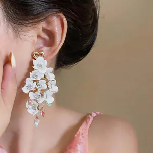 Detailed close-up of white fabric flower tassel earrings with heart stud