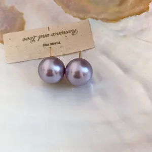 Close-up view of elegant purple pearl stud earrings displayed on a textured fabric card