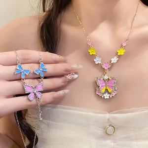 Detailed macro view of a colorful gold-tone butterfly and flower pendant necklace worn by a model.