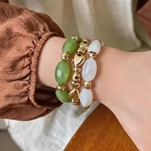 Stapelbare Acrylperlenarmbänder mit Herz- und Ovalformen in Grün, Gold und Weiß.