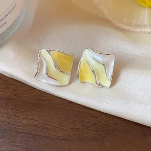 Primo piano di orecchini geometrici a pieghe gialli e crema su tessuto di seta.