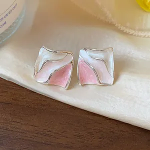 Primo piano di orecchini geometrici a pieghe in smalto rosa e bianco su seta