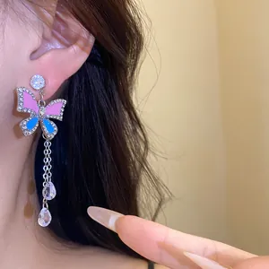 Macro view of color contrast butterfly tassel earrings with crystal rhinestones on ear.