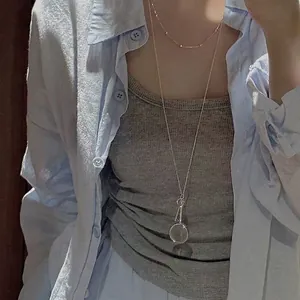 Close-up detail of magnifying glass and key pendant on a long silver necklace for women