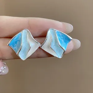 Dettaglio degli orecchini geometrici in smalto blu e bianco con design a onde