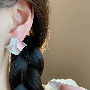 Primo piano di eleganti orecchini a perno geometrici in smalto rosa su un orecchio.