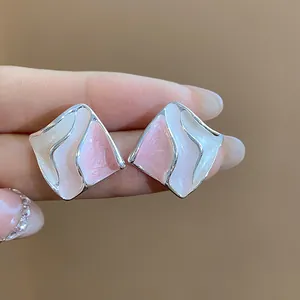 Vista macro dettagliata di orecchini a lobo geometrici in smalto rosa e bianco per l'estate