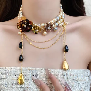 Gros plan d'un collier de perles vintage avec fleurs métalliques et pendentifs en goutte.
