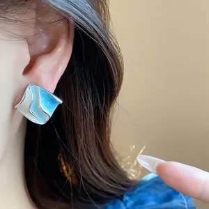 Primo piano di orecchini geometrici in smalto blu sull'orecchio di una modella.