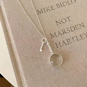 Detail view of silver necklace featuring magnifying glass and key charms on a vintage book.