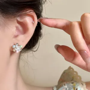 Dettaglio ravvicinato di un orecchino a uva in argento con perle e strass colorati brillanti.
