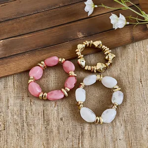 Drei stilvolle geometrische Acryl-Armbänder mit goldfarbenen Akzenten auf rustikalem Grund.