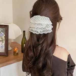 Detailaufnahme einer eleganten weißen Spitzen-Haarklammer mit Perlen auf braunem Haar.