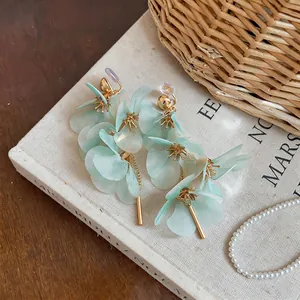 Detailed view of mint green petal drop earrings with gold bar tassels on vintage book