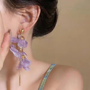 Close-up of elegant long dangling earrings with purple floral petals on an Asian model
