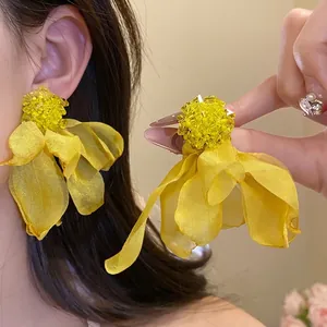 Elegant yellow chiffon flower stud earrings with beaded centers, worn by a model.