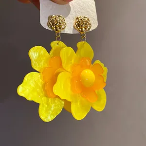 Primer plano de pendientes de flores de resina amarilla con tachuelas de rosas doradas
