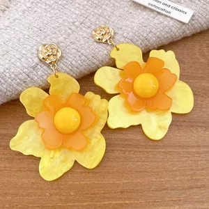 Primer plano detallado de pendientes de flores de resina en tonos amarillos y naranjas.