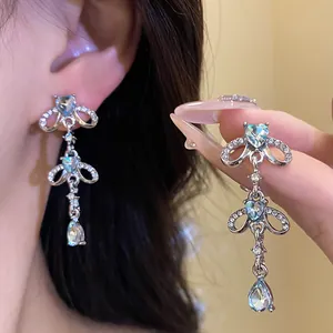 Detailed macro view of sparkling heart and teardrop tassel earrings worn by a model
