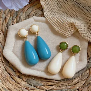 Minimalist resin waterdrop stud earrings in blue and cream colors on a rustic background.
