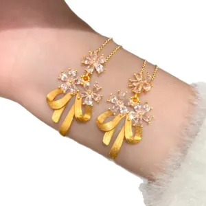 Elegant 24k gold-plated necklace featuring sparkling zircon flower and bow pendants on arm.