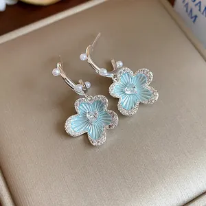 Detailed macro shot of light blue enamel flower earrings featuring heart zircon and pearls.