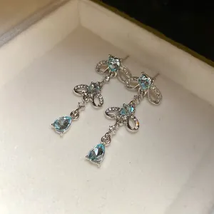 Close-up of elegant silver bow tassel earrings featuring light blue heart and teardrop stones.