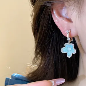 Detailed close-up of a blue enamel flower earring with zircon and pearls on a model ear.