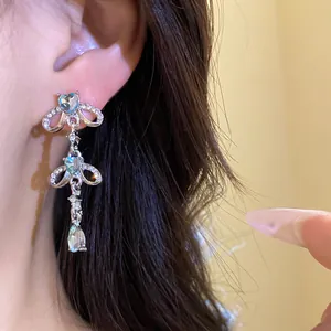 Detailed view of silver-tone tassel earrings with heart and drop blue stones on ear.