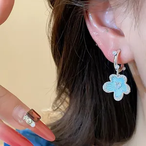 Detail showing a blue enamel flower earring with pearl and zircon accents on a model's ear