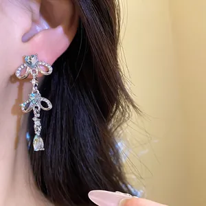 Close-up detail showing a silver-tone earring with rhinestone heart and waterdrop tassels