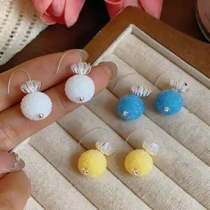 Close-up detail of textured round glass ball pendant earrings with elegant flower caps