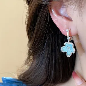 Close-up of elegant blue oil-dripped flower earring with pearls and zircons on ear
