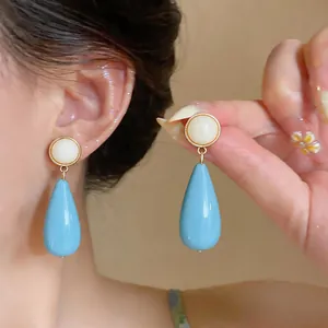 Elegant minimalist light blue resin teardrop earrings shown on model for high-end fashion appeal.