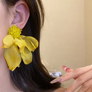 Close-up of oversized yellow chiffon flower earrings with beaded center on a model