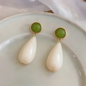 Detail view of minimalist resin teardrop earrings with green stud and cream drop.