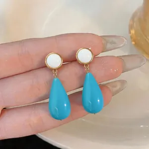 Close-up detail of trendy blue resin teardrop earrings with white circular studs.