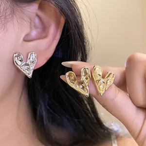 Elegant minimalist irregular metal heart stud earrings shown on ear and held by hand