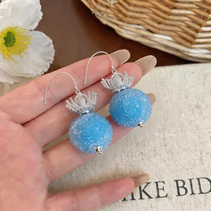 Macro detail of elegant light blue glass flower round drop earrings held in hand