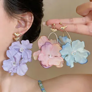 Macro detail of elegant fabric flower earrings in purple, pink, and blue with gold bird