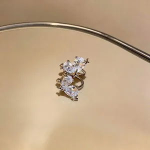 Detail of sparkling pear-cut zircon heart ear cuffs with cross accents on gold surface