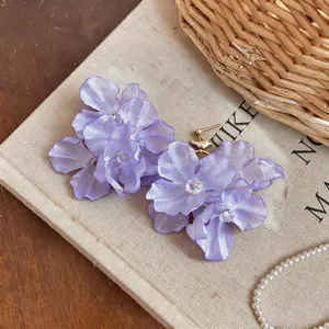Detail of elegant purple fabric flower earrings with crystal center on canvas.