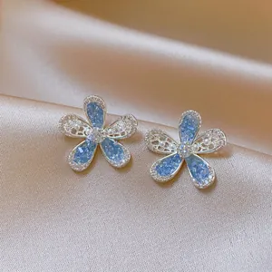 Close-up detail of silver-toned flower stud earrings with blue stones and small pearls