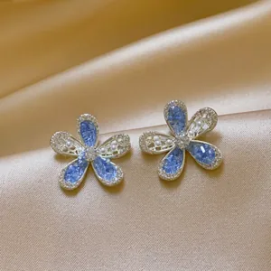 Close-up of elegant blue hollow-out flower stud earrings with sparkling crystals and pearls