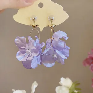 Close-up of elegant purple fabric flower earrings with a delicate gold bird accent
