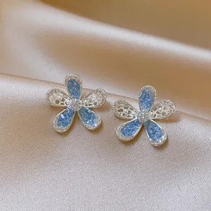 Close-up of blue hollow flower stud earrings with rhinestones on satin background.