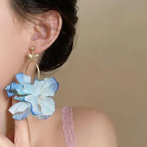 Close-up of large blue fabric flower earrings with gold bird detail on an Asian model.