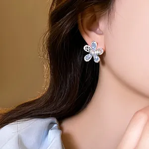 Detail of blue hollow flower stud earrings with rhinestones on an Asian female model.