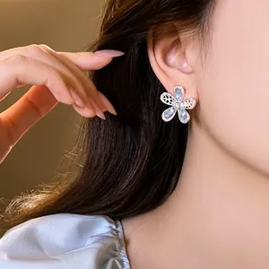 Detailed view of hollow-out flower earring with blue crystals on an Asian model