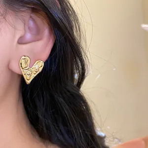 Close-up of a minimalist gold metallic heart earring with a textured lava finish